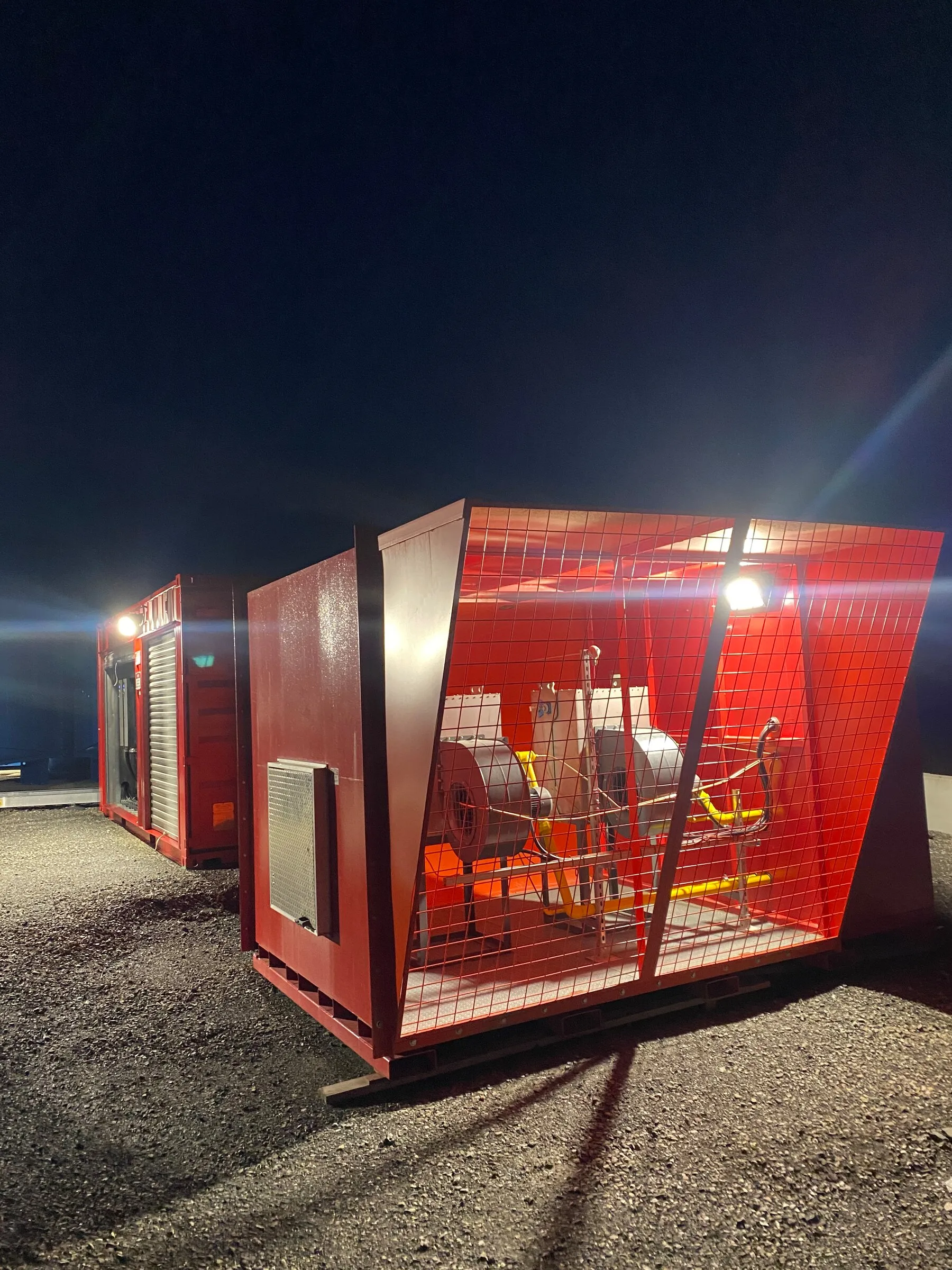 Deux réchauffeurs d’air miniers en marche la nuit sur une plateforme de gravier éclairée par des projecteurs, sur un site minier