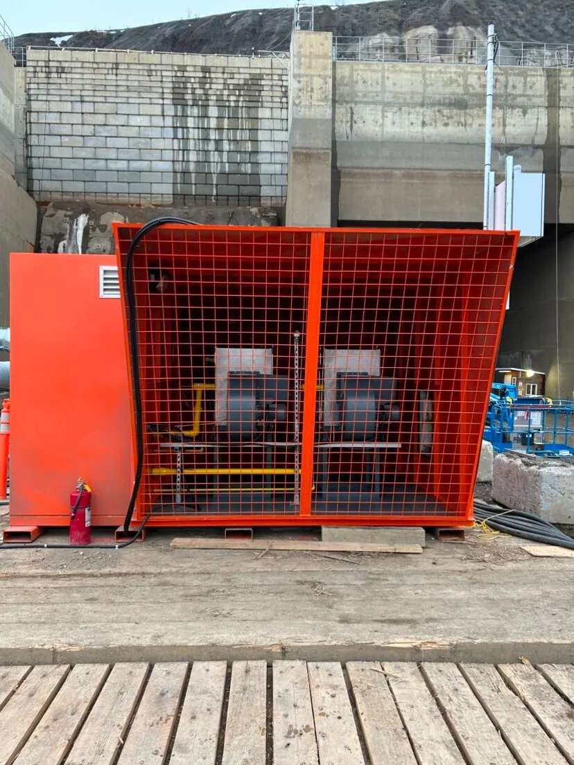 Réchauffeur d’air minier grillagé installé sur une plateforme de bois, à côté d’un mur de soutènement en béton